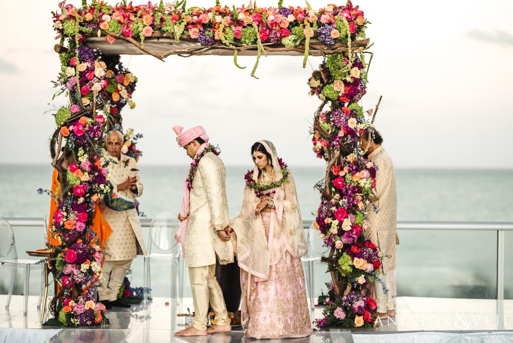 A wedding ceremony taking place on an outdoor patio with a floral archway and ocean views.