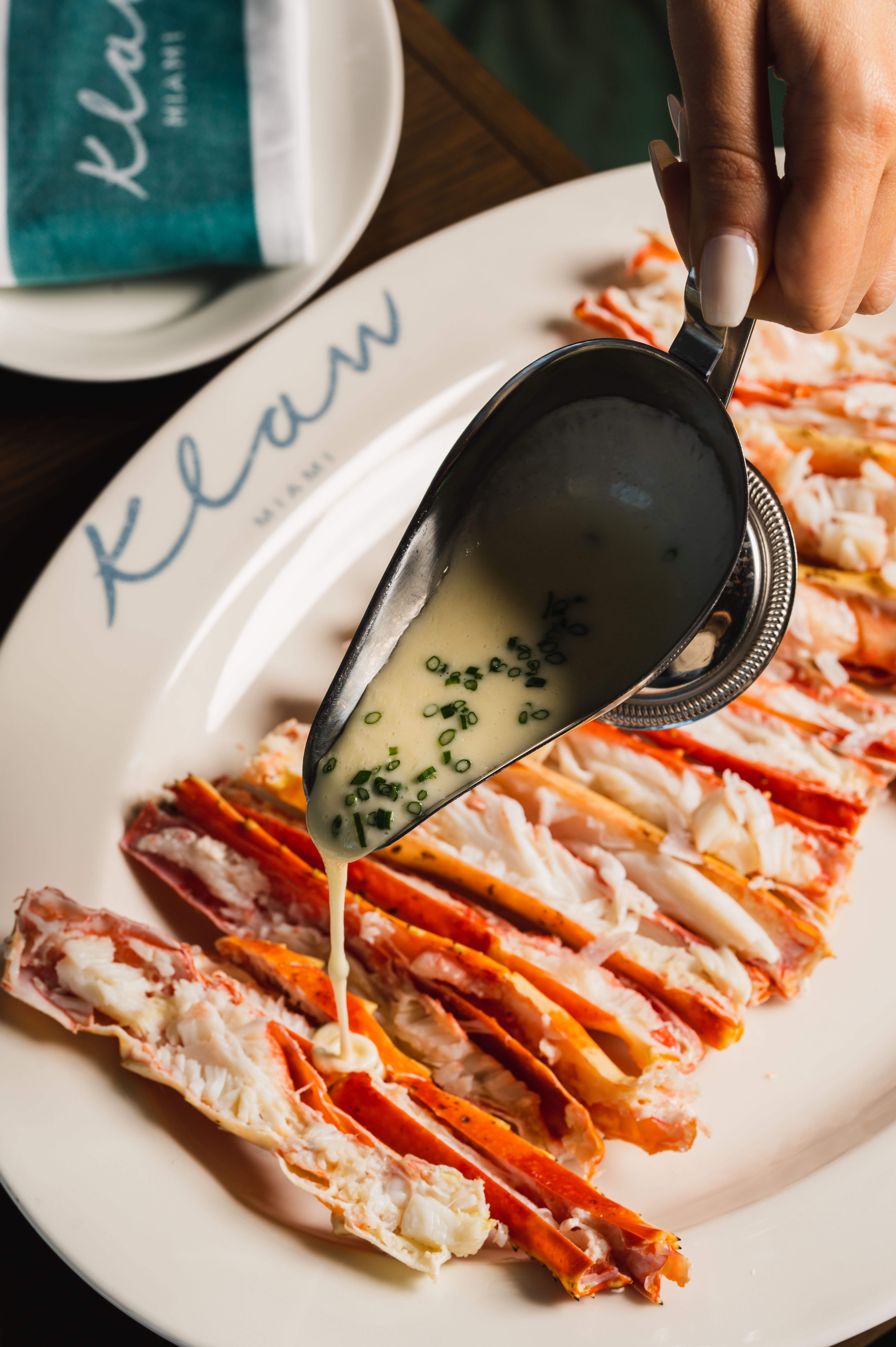 A hand pouring a creamy sauce over a plate of crab.