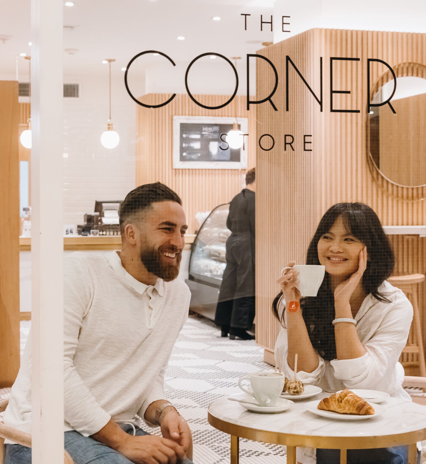 A couple sits at a small table in a restaurant, enjoying coffee and pastries.